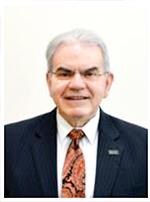 a headshot of a man. He is wearing a dark blazer and a reddish tie.