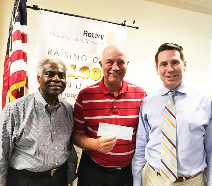 Three men stand side by side. They are presenting a typical sized check to the camera. 