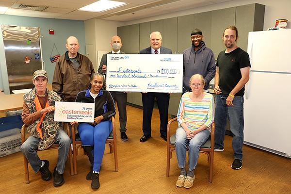 Seniors and adults with acquired disabilities stand with two CEO's as a large check is being presented