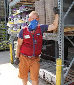 A Lowes employee stands in the garden center and looks at the camera with a blue mask on