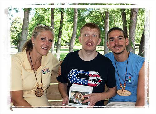 A camp director and counselor sit on either side of a man with a disability at a Campground