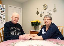 Older couple sits at dining room table and hold hands