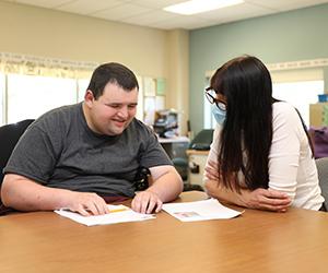 Man with a disability sits at a table with his direct support professional