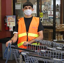 Employee wearing a mask is wearing an orange vest and has his hands resting on shopping carts