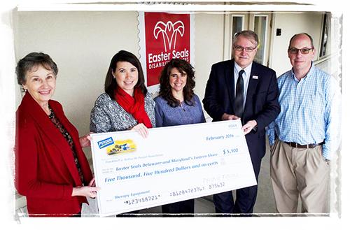 five adults stand in front of an Easterseals sign while holding a large check