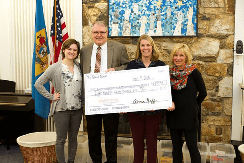 Four people stand in front of a stone wall presenting a check to the camera. 