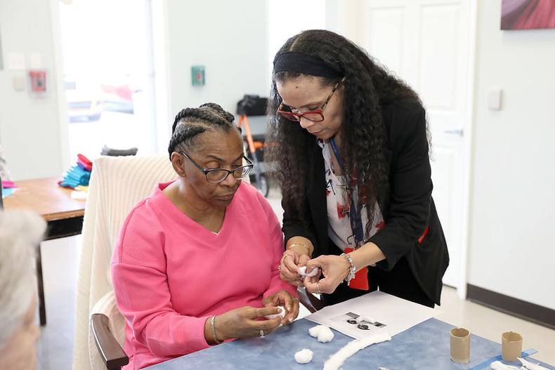 A senior woman making crafts with an assistant