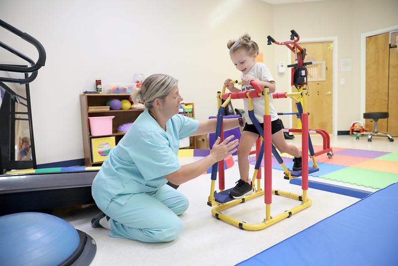 A child with disability runs on a device while phyiscal therapist assists