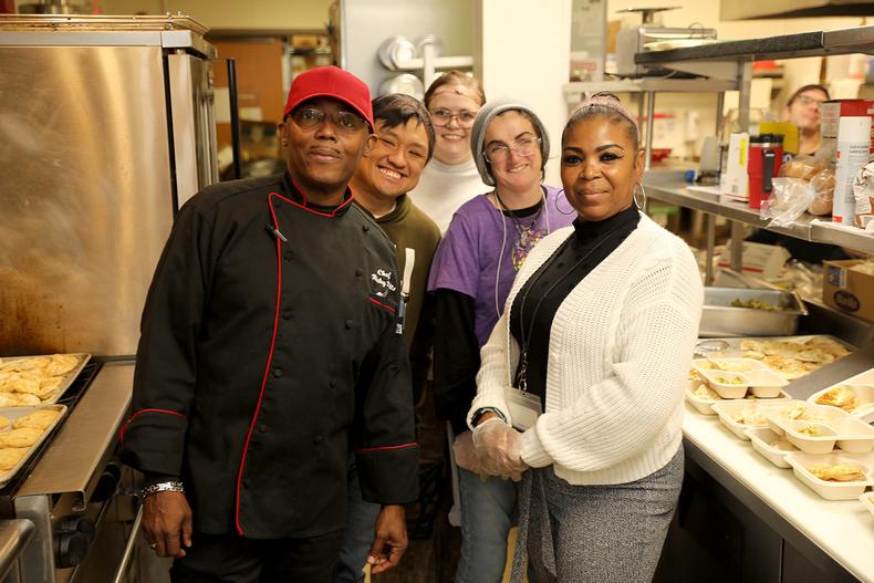 A group of people stand in a kitchen and they are all smiling at the camera