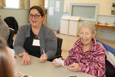 A volunteer smiles and laughs at a table with a senior as they are both playing cards