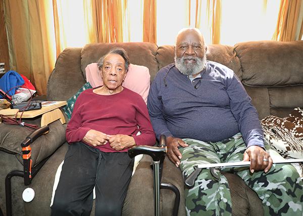 An older couple sits on a couch and looks at the camera