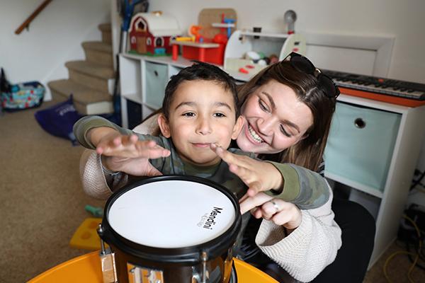 A child with autism play a drum with the assistance of a therapist