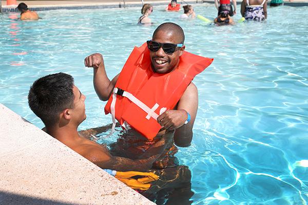 A man with a disability is swimming in a pool with the assistance of his counselor