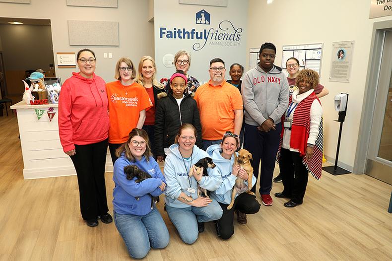 A group of people and dogs stand in an animal rescue center and smile at the camera.