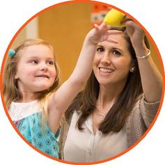 Child reaching for a yellow toy as her therapist works with her