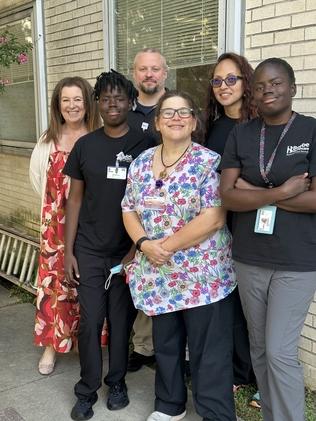 A group of people in hospital scrubs and work uniforms posing in front of a wall