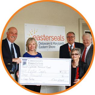 Five individuals are standing in front of an Easterseals logo on the wall. They are presenting a large check to the camera. 