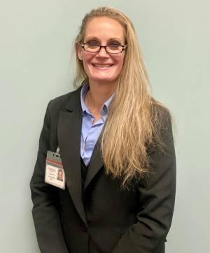 A woman with long blonde hair, wearing a black blazer smiles at the camera