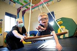 Child with disability on a physical therapy swing with therapist pushing him.