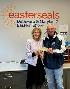 Two people stand in front of an Easterseals sign and hold up a check donation.