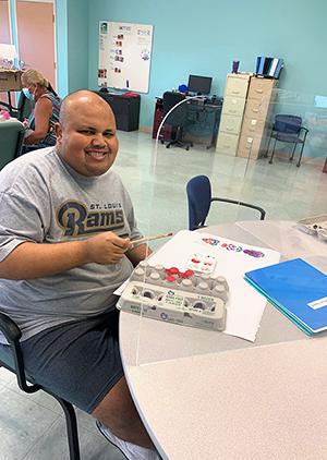 A person with a disability paints egg cartons and smiles to the camera