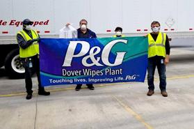 A group of employees wearing masks all stand together holding up a large sign