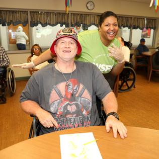 A man with a bucket hat smiles at the camera as a volunteer behind him smiles