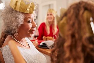 A woman with a gold paper crown smiles at a dining room table during the holidays