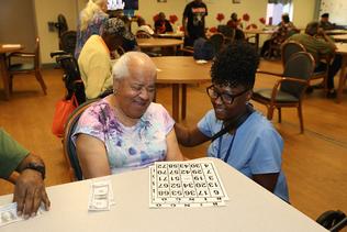 A blind senior and an assistant smile at each other while playing bingo.