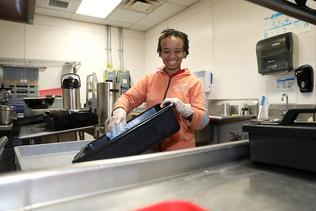 A woman with a disability stands in a kitchen and washes dishes