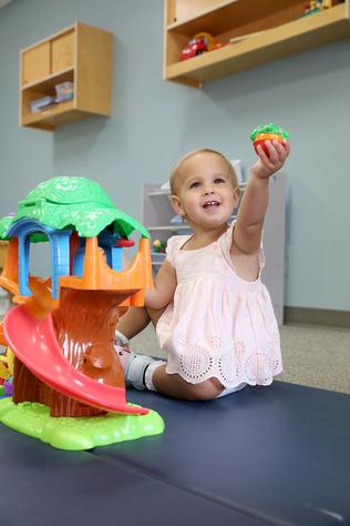 A toddler smiles as she holds a colorful toy into the air.