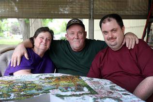 Older parents sitting at a table doing a puzzle with their adult son that has a disability