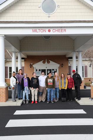 A group of people stand in front of a building that says Milton Cheer