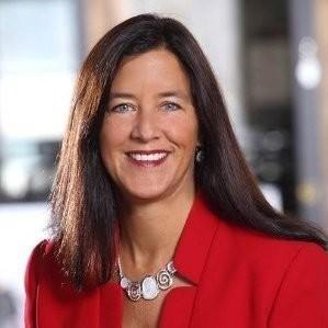 A headshot of a woman with long brown hair, wearing a red jacket and smiling at the camera