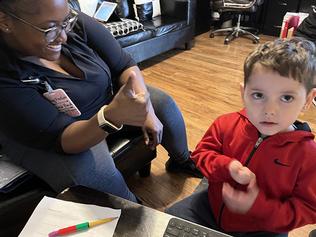 A child looking at the camera while his therapist smiles at him with a thumbs up.