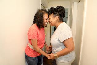 Woman with a disability is smiling and embracing her mother in a hallway. 