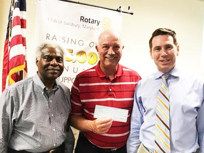 Three men stand side by side. They are presenting a typical sized check to the camera. 