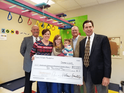 A group of people stand in a Children's Therapy Gym presenting a large check.