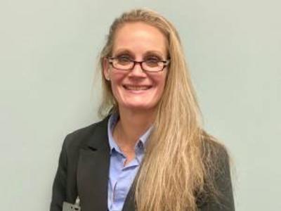 A woman with long blonde hair, wearing a black blazer smiles at the camera