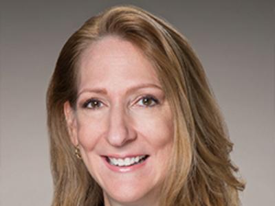 A Headshot of a woman with long hair. She is wearing a black blazer.