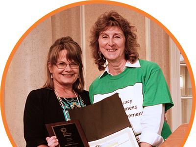 Two women are holding a signed resolution and smiling at the camera