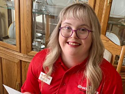 Woman with Down Syndrome wearing a Grottos Pizza Polo smiles at the camera