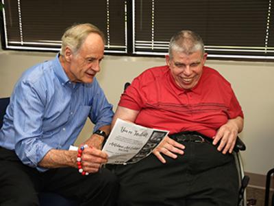 Legislator reads from paper while talking to a participant who is blind and has a hearing impairment