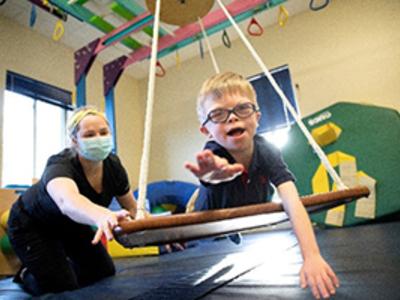 Child with disability on a physical therapy swing with therapist pushing him.