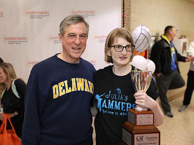 Person with disability holds a trophy and poses with elected official at volleyball event