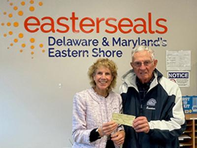 Two people stand in front of an Easterseals sign and hold up a check donation.