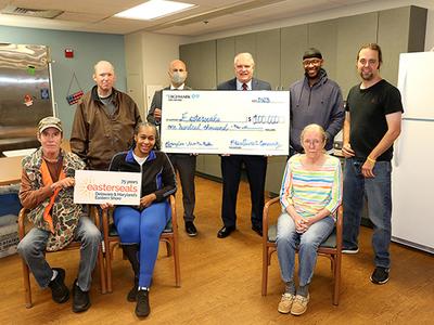 Seniors and adults with acquired disabilities stand with two CEO's as a large check is being presented