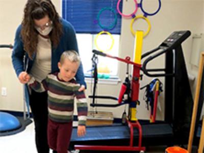 A child with a disability walks along a circular beam as a therapist assists him.