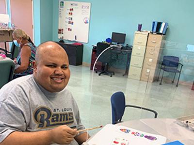 A person with a disability paints egg cartons and smiles to the camera