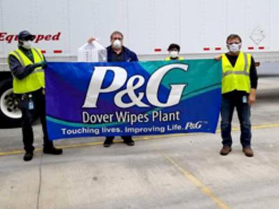 A group of employees wearing masks all stand together holding up a large sign